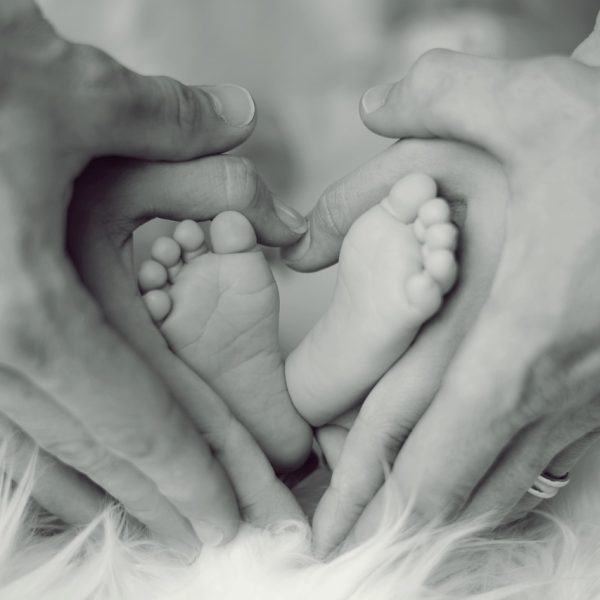 Pieds d’un bébé tenus par les mains de ses parents, symbolisant le modelage bébé proposé par le Centre de soins Naxane pour renforcer le lien parent-enfant.