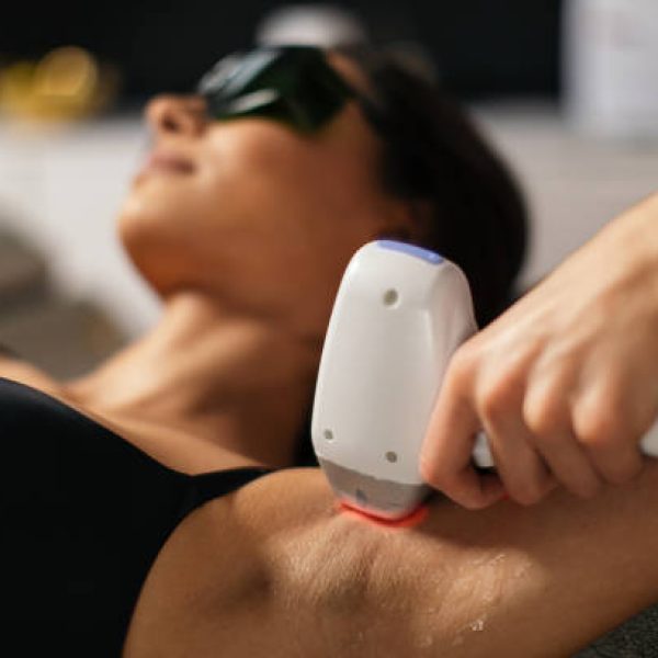 Attractive young woman receiving body hair removal treatment with laser in beauty, anti age, health and body care clinic. Beautician is holding laser device and doing epilation on armpit